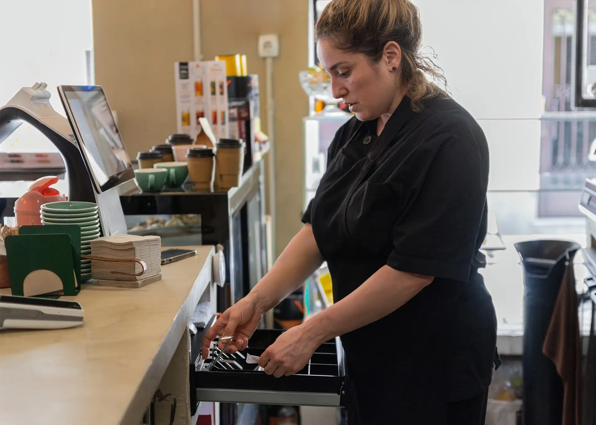 barista handling cash at POS till in busy cafe environment